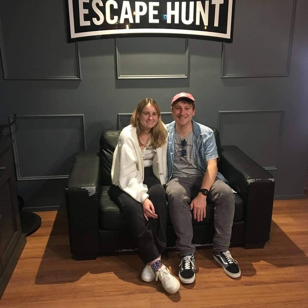 Maggie and Jack sitting on a couch under an Escape Hunt sign